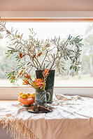 Vase with banksia branches and fruit bowl on windowsill