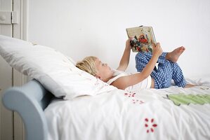 Little boy lying down on his bed reads a book
