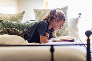 Dreizehnjähriges Mädchen liegt auf dem Bett und liest beim Tageslicht