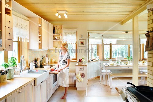 Offene Küche mit heller Holzdecke, Frau mit Schürze vor Küchenzeile, im